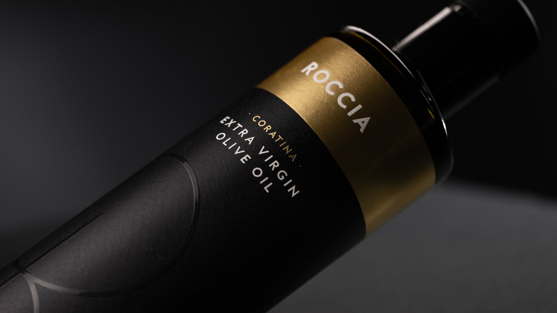 Olio Roccia Coratina extraszűz olívaolaj palackja arany címkével, sötét háttér előtt